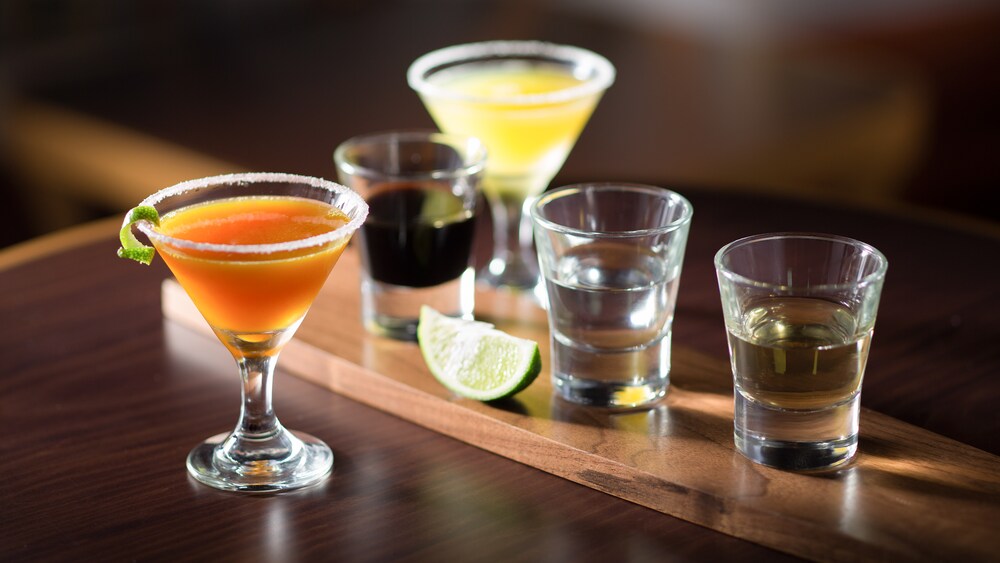 3 shots of various tequilas next to 2 glasses containing two types of margaritas