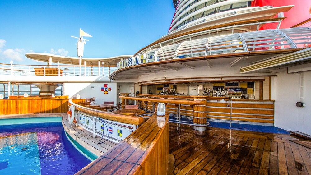 An outdoor bar is on a deck next to a large swimming pool