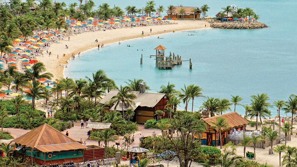 A crescent shaped beach area features cabanas, lots of umbrellas and crystal clear water