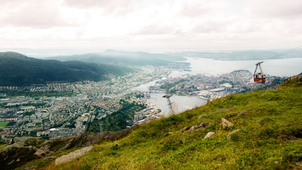 A cable car is supended over a coastal city with hillsides rolling into the background