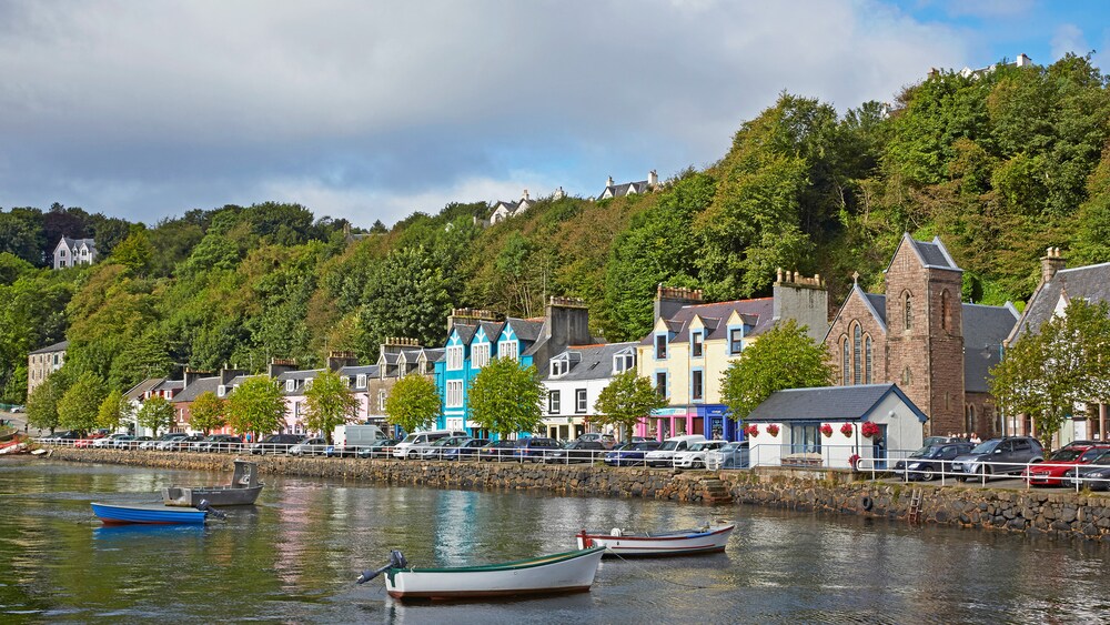 Row houses and trees line a harbor containing several small boats in Inner Hebrides, Scotland