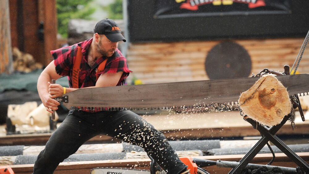 Lumberjack with a sleveless shirt pulls a band saw across a log