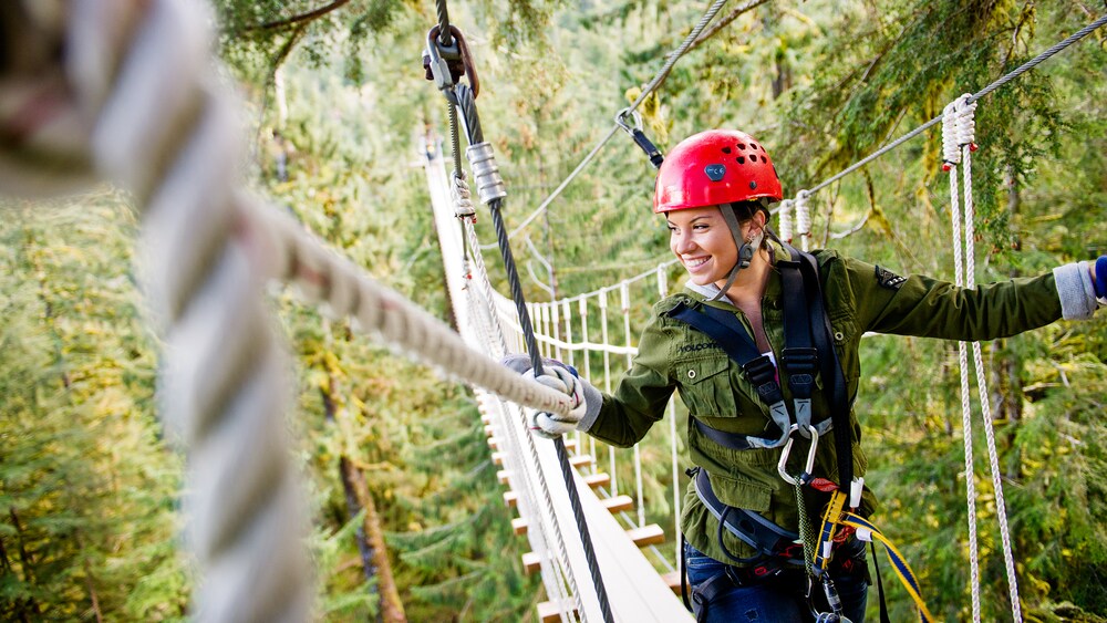 Smiling woman in safety harness standing on a rope bride suspended in the trees