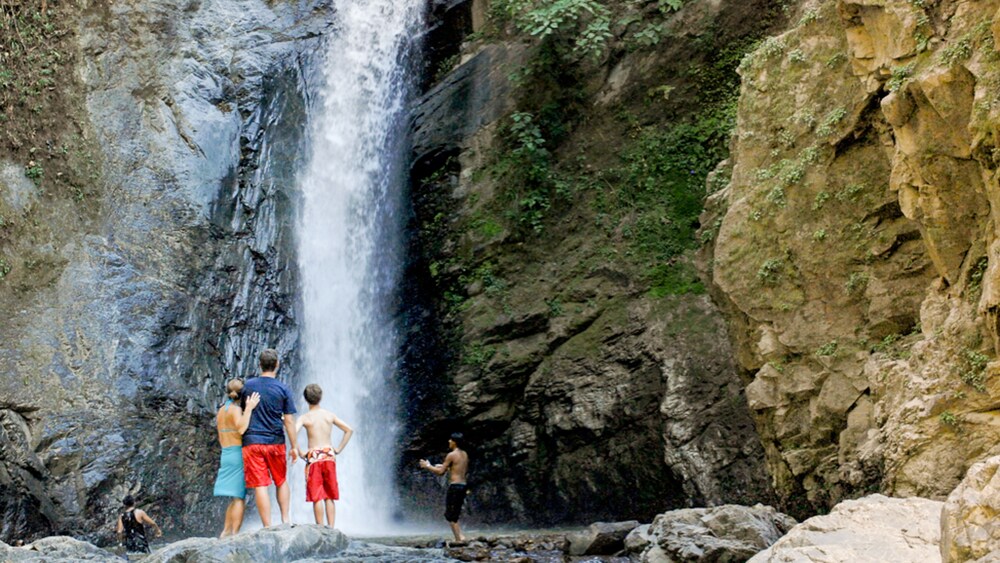 People stand in front of a tall waterfall pouring down a rock face