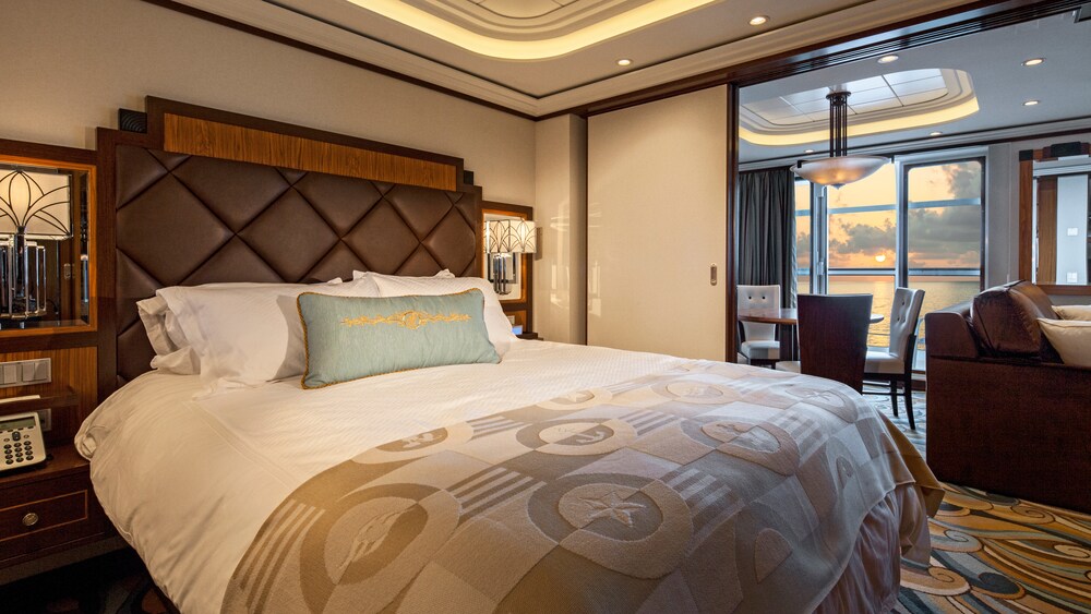 A Disney Cruise Line Concierge 1 Bedroom Suite with Verandah Stateroom with a bed, a dining table, a verandah with an ocean view and a sofa