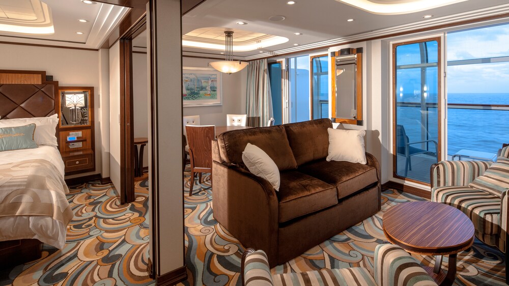 A Disney Cruise Line Concierge 1 Bedroom Suite with Verandah Stateroom with a bed, a dining table, a verandah with an ocean view, a sofa, a chair and a low table