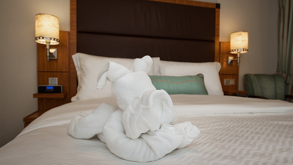 A Disney Cruise Line Concierge Verandah Stateroom with a bed, 2 wall sconces and a chair