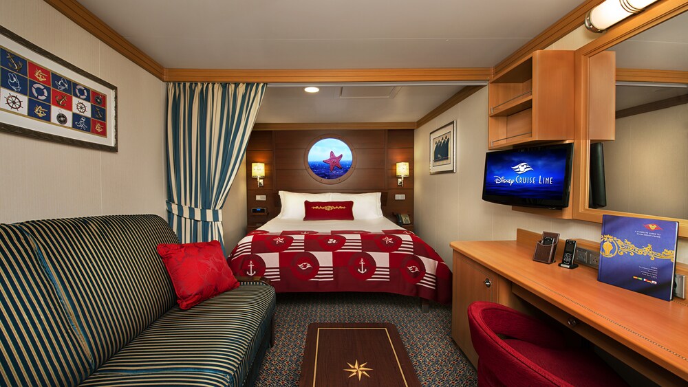 A Disney Cruise Line Deluxe Inside Stateroom with a low table, a sleeper sofa, a bed, a virtual porthole, storage shelves, a TV, a mirror and a desk