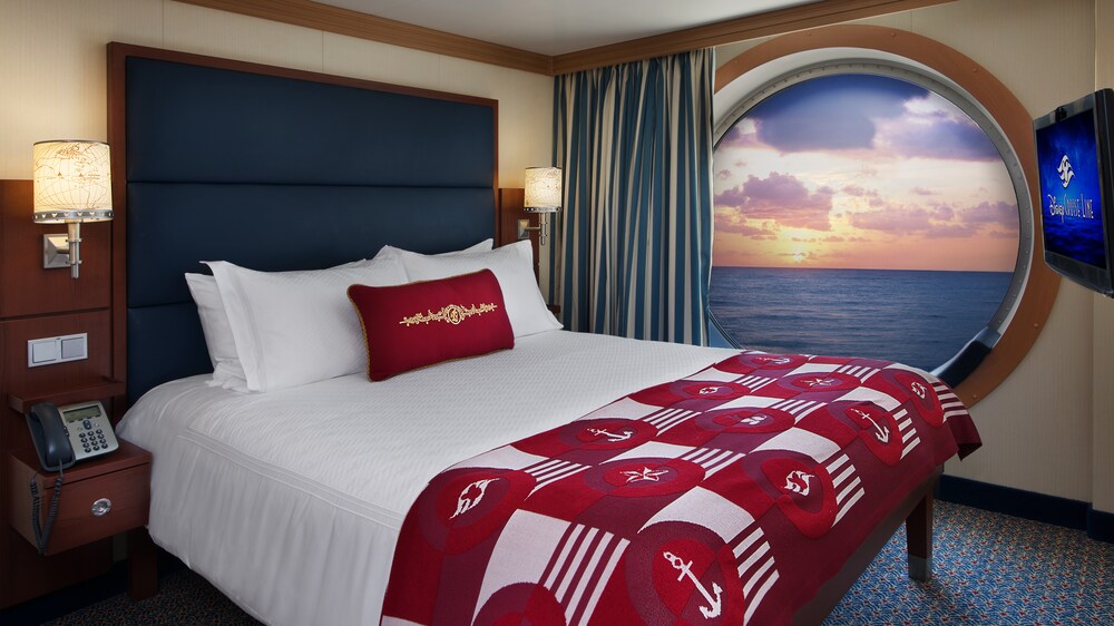 A bed next to a floor to ceiling porthole, revealing a sunset