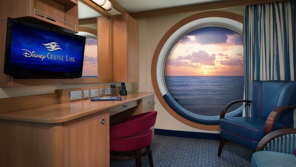 A desk next to chairs and a floor to ceiling porthole, revealing a sunset
