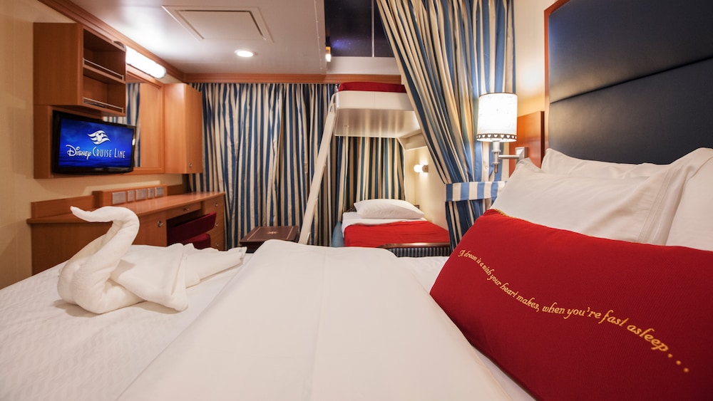 A Disney Cruise Line Deluxe Oceanview Stateroom with a desk, storage shelves, a porthole with an ocean view, a sofa and a bed