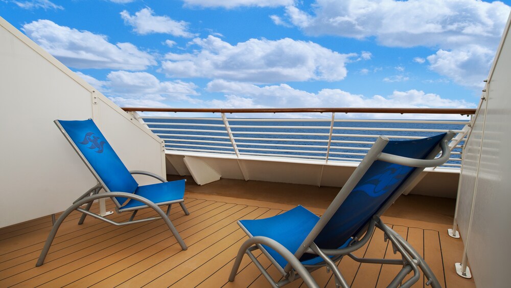 Two opposing deck chairs on a verandah, with partitions on either side and a railing with an ocean view