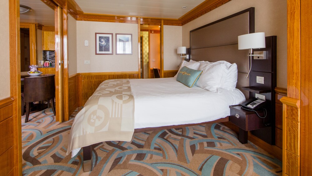A Disney Wonder Concierge 1 Bedroom Suite with Verandah living room with a sofa, TV, side table, dining table and chairs