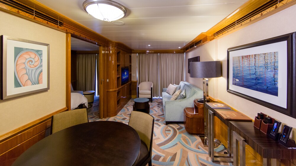 A Disney Wonder Concierge 1 Bedroom Suite with Verandah living room with a sofa, TV, side table, dining table and chairs