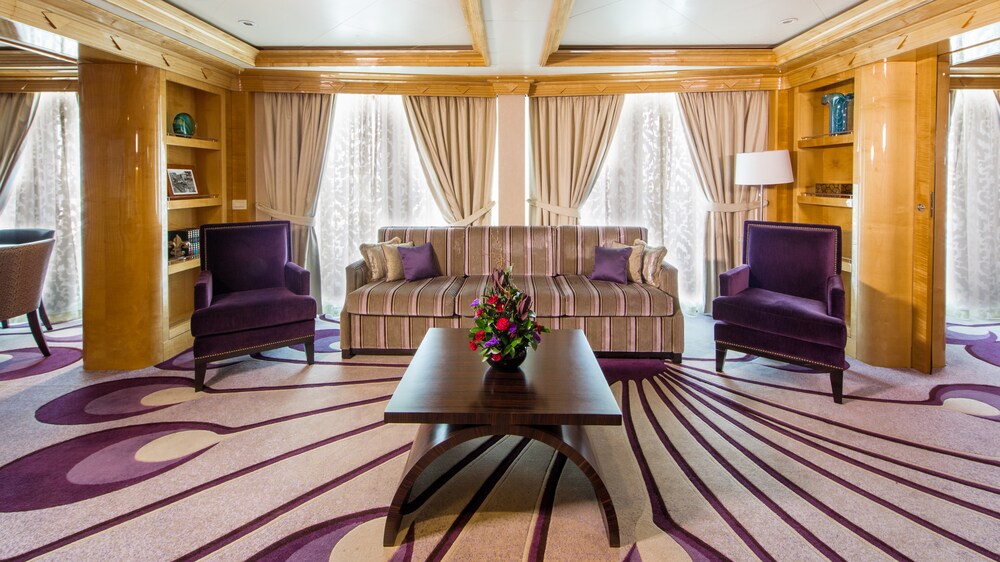 A Disney Cruise Line Concierge Royal Suite with Verandah living room with a sofa, a table, 2 chairs and shelves