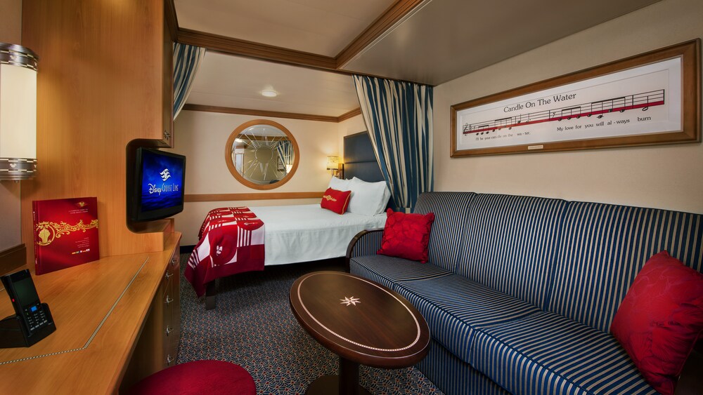 A Disney Cruise Line Deluxe Inside Stateroom with a bed, sofa, table, desk, TV and mirror