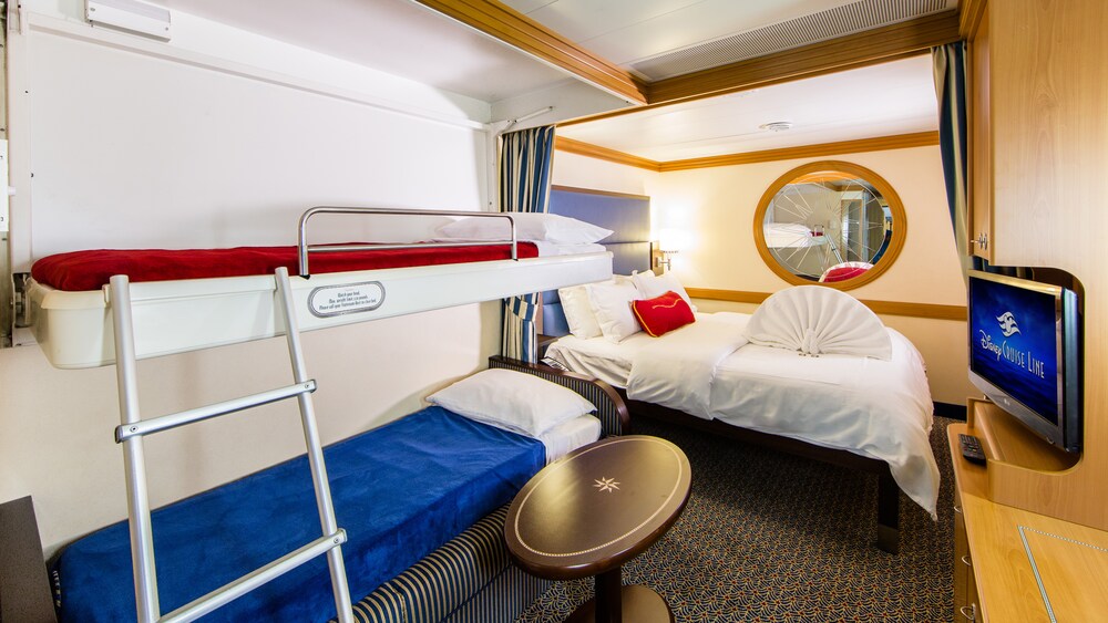 A Disney Cruise Line Standard Inside Stateroom with a bed, sofa, table, desk, TV and mirror