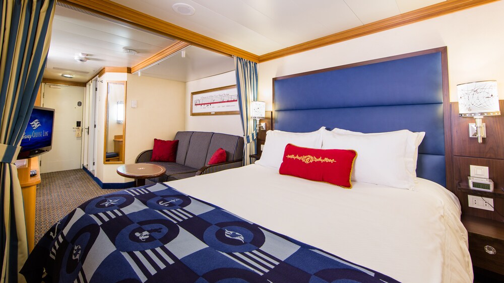 A Disney Cruise Line Standard Inside Stateroom with a bed, sofa, table, desk, mirror, TV and a nightstand