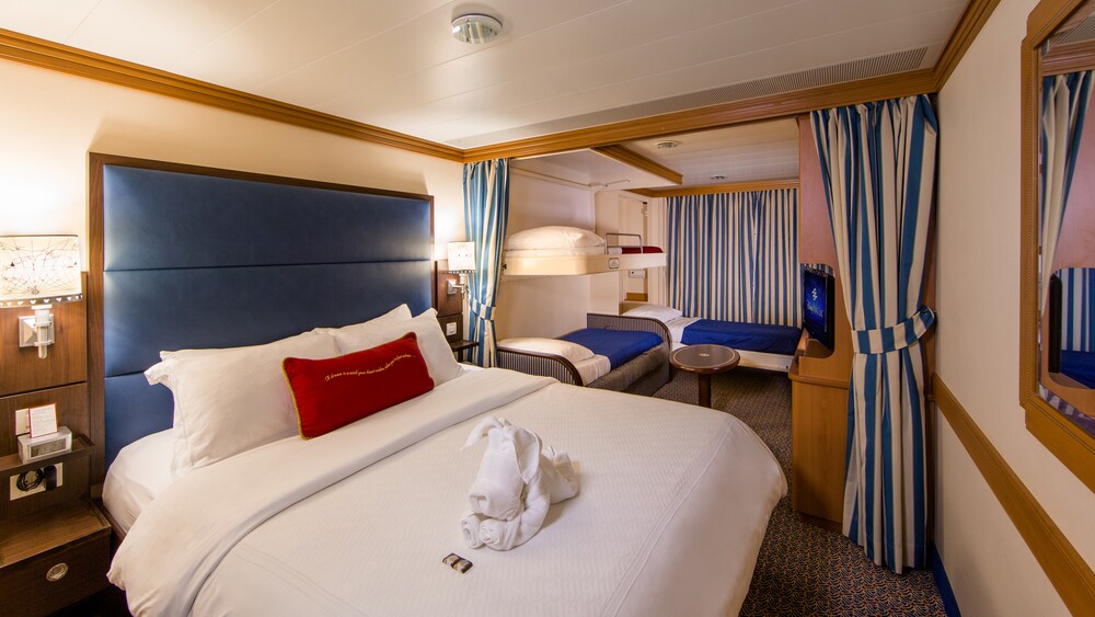 A Disney Cruise Line Deluxe Family Oceanview with Verandah Stateroom with a bed, sofa, chair, table, desk, TV, 2 nightstands and a verandah facing the ocean