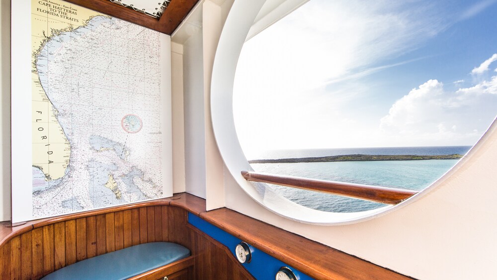A wood sauna with a bench, below a map of Florida and next to an oval opening with a view of the ocean