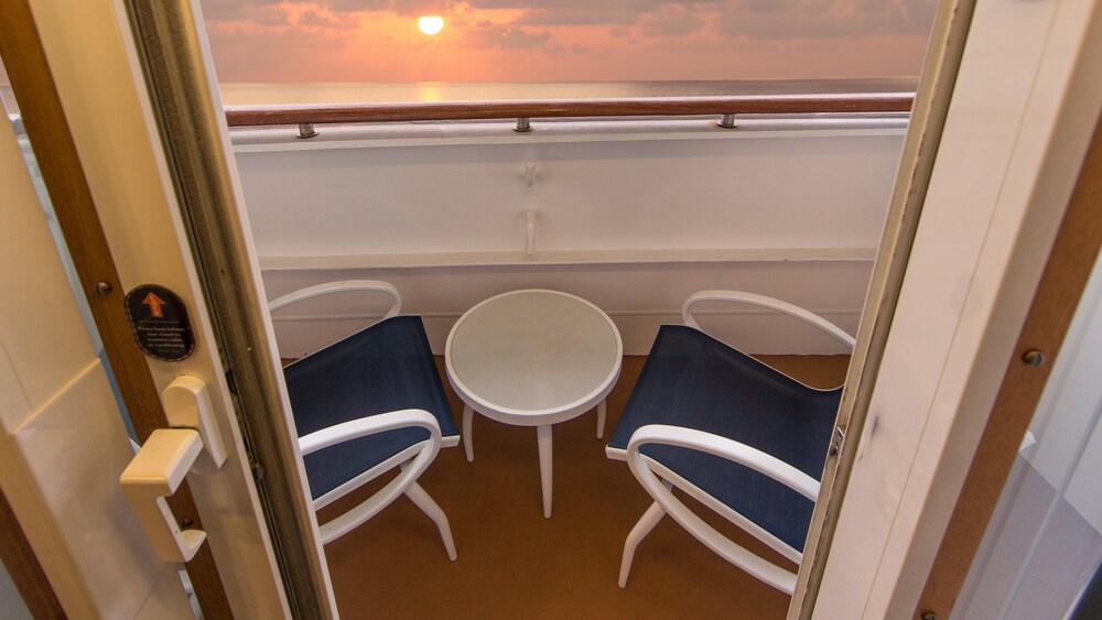A Disney Cruise Line stateroom verandah facing the ocean with 2 chairs and a table