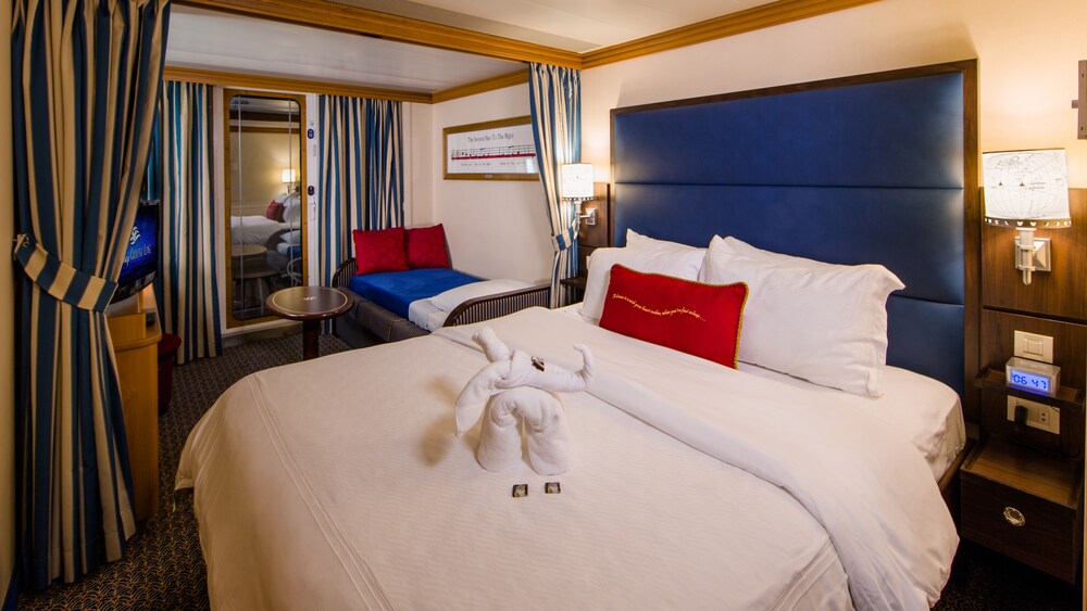 A Disney Cruise Line Deluxe Family Oceanview with Verandah Stateroom with a bed, sofa, chair, table, desk, TV, 2 nightstands and a verandah facing the ocean