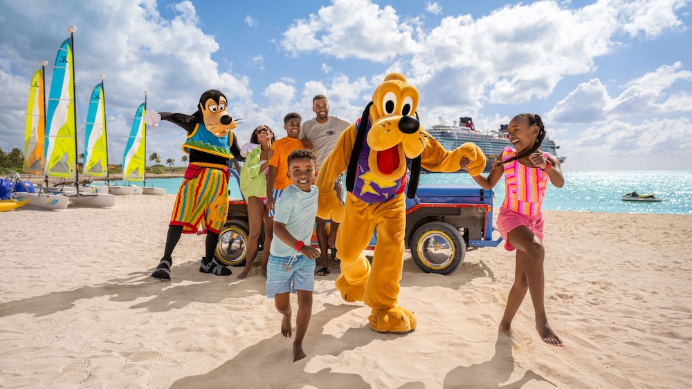 A family holding hands and running on the beach with Goofy and Pluto