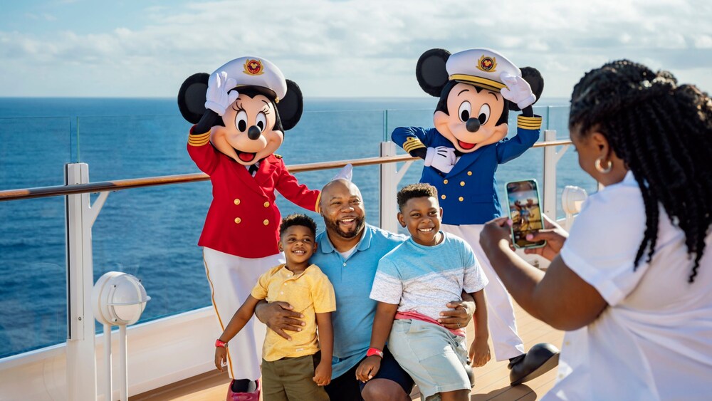 A father and his two sons smile and pose for a photo on a boat with Mickey Mouse and Minnie Mouse