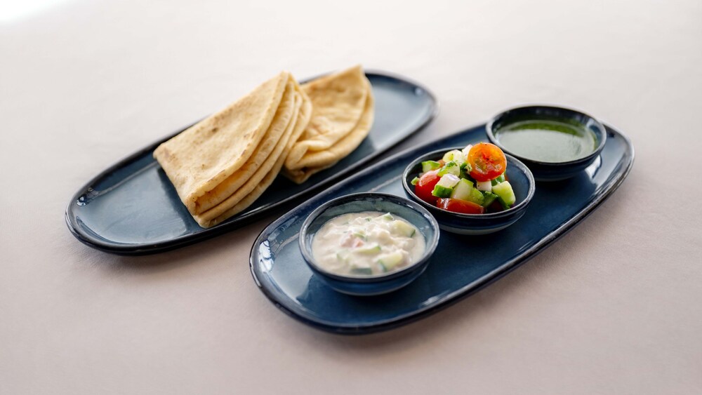 Two plates, one with pita bread and the other with dipping sauces and a mixed vegetable topping
