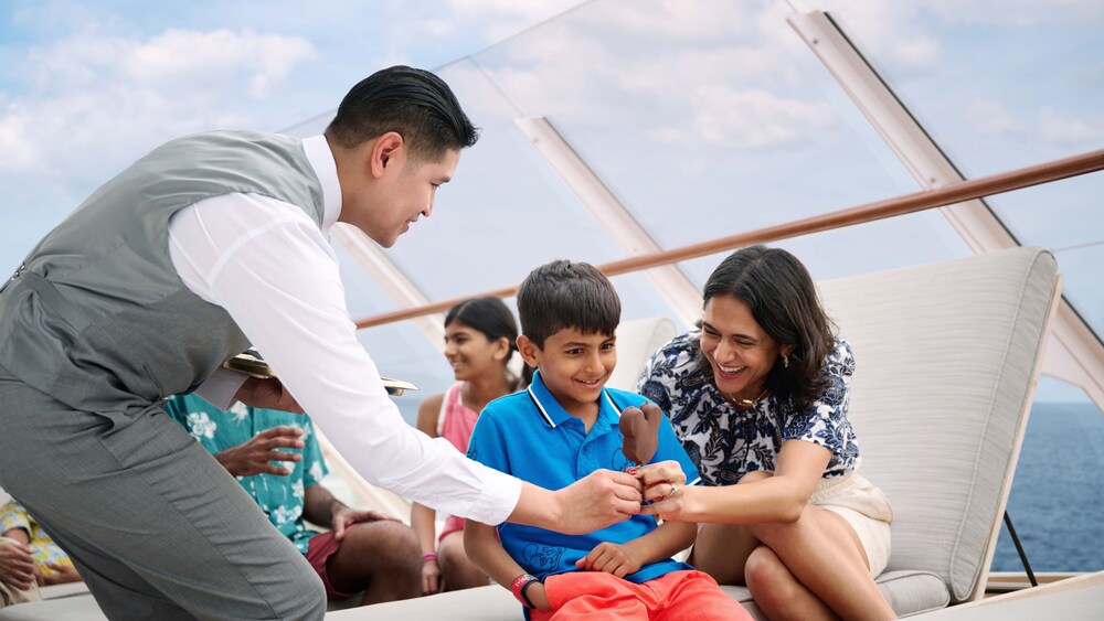 A young boy and his mother sitting on a lounge chair, being handed an ice cream bar by a Cast Member
