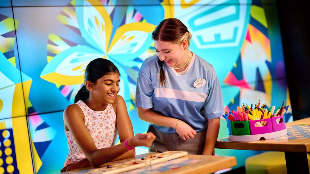A young girl sitting at a table with a game while talking to a Cast Member