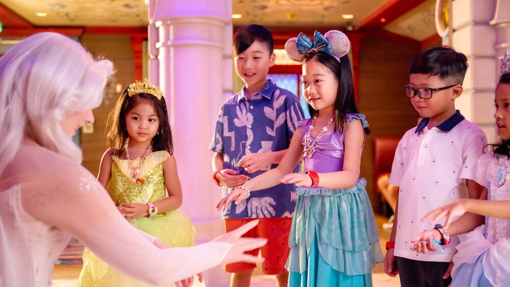 Three girls wearing Disney Princess dresses and 2 boys talking with Elsa
