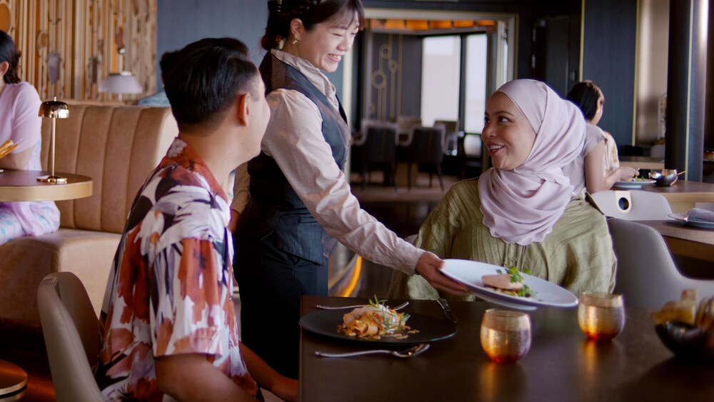 A Cast Member serves food to a couple at a restaurant on a Disney Cruise Line ship 