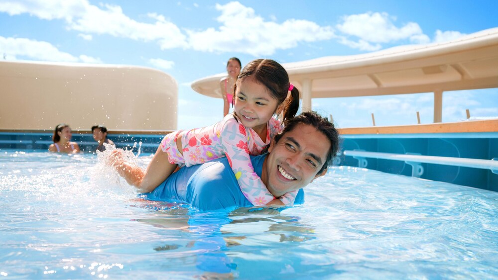 A young girl riding on her father's back in a pool