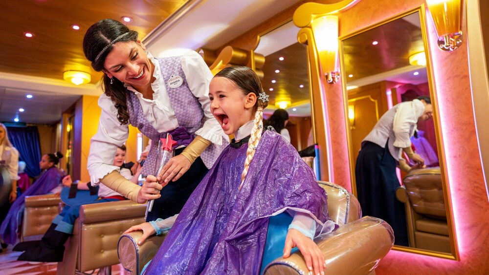 A young girl in a salon chair being served by a Cast Member at the Bibbidi Bobbidi Boutique