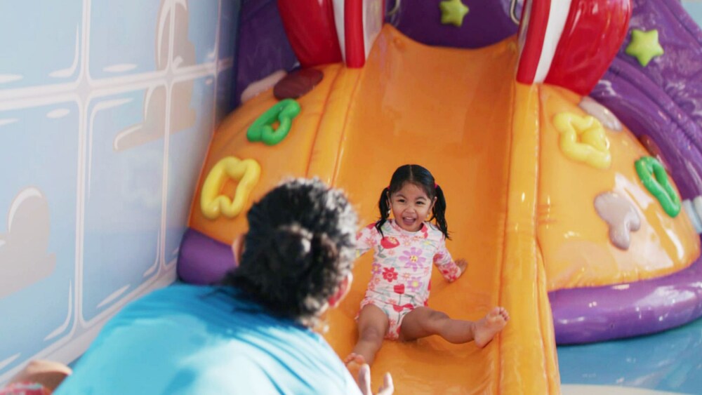 A young girl smiling and riding down a slide towards a waiting adult
