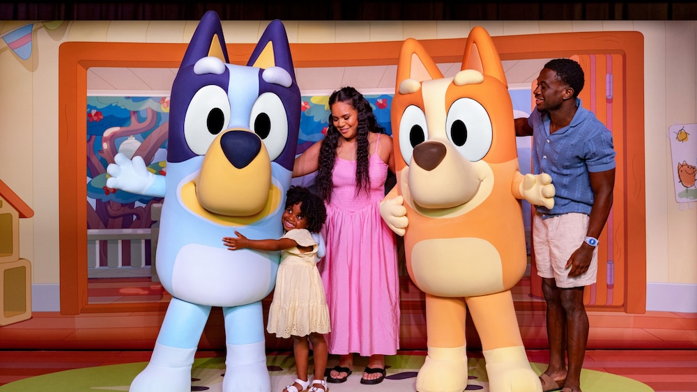 A family of 3 posing for a photo with Bluey and Bingo while on a Disney Cruise ship