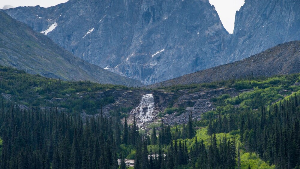 Alaskan landscape featuring rocky mountains, a cascade and a forest in Skagway