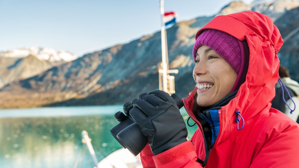 A woman holding a pair of binoculars while admiring the glacier views of Alaska
