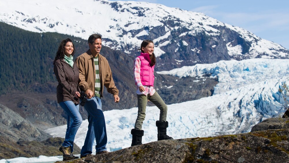 A family of 3 standing on an outcrop in the Alaskan mountains