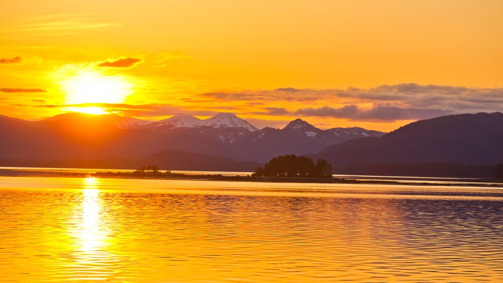 A sunset over a body of water and snow capped mountains in Southeast Alaska.