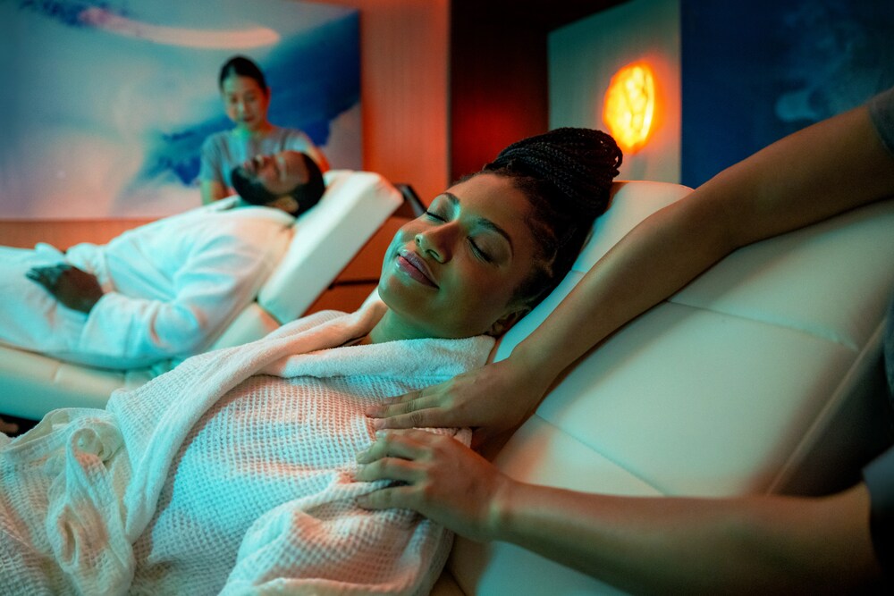 Un hombre y una mujer con los ojos cerrados recibiendo un masaje en sillas de masaje reclinables.