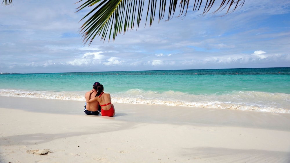 A couple sitting on the sand at Serenity Bay on Disney Castaway Cay, gazing at the water
