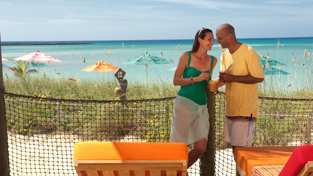 A couple enjoying drinks at Serenity Bay on Disney Castaway Cay, with umbrellas and water in the background