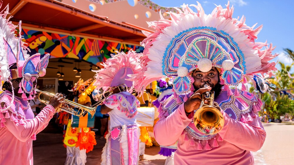 Un hombre tocando una trompeta en un desfile mientras viste ropa festiva bahameña.