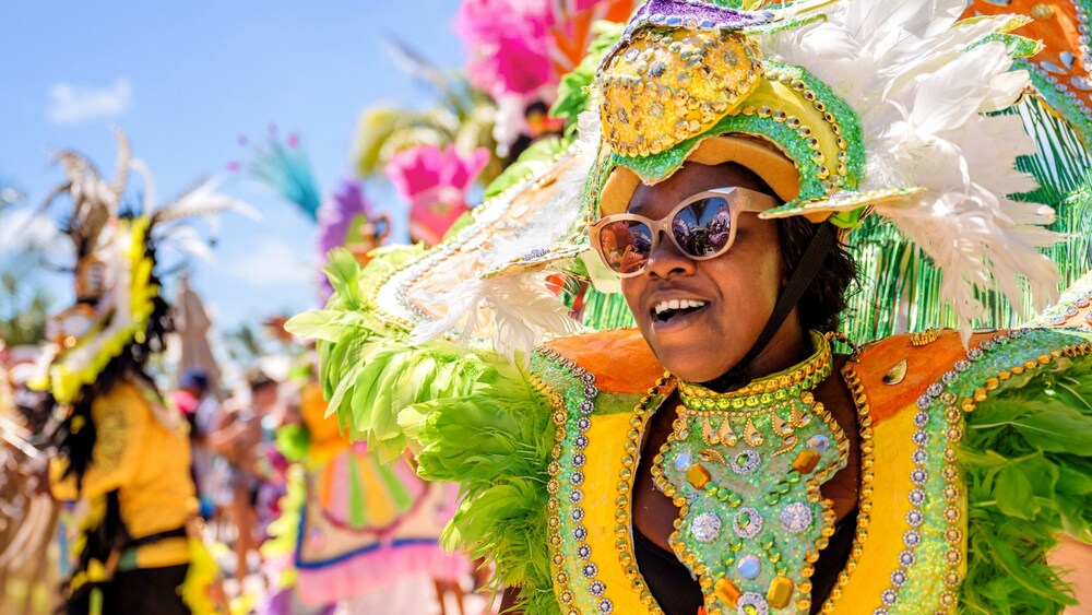 Una mujer con anteojos de sol y sonriendo en un desfile vestida con ropa festiva bahameña