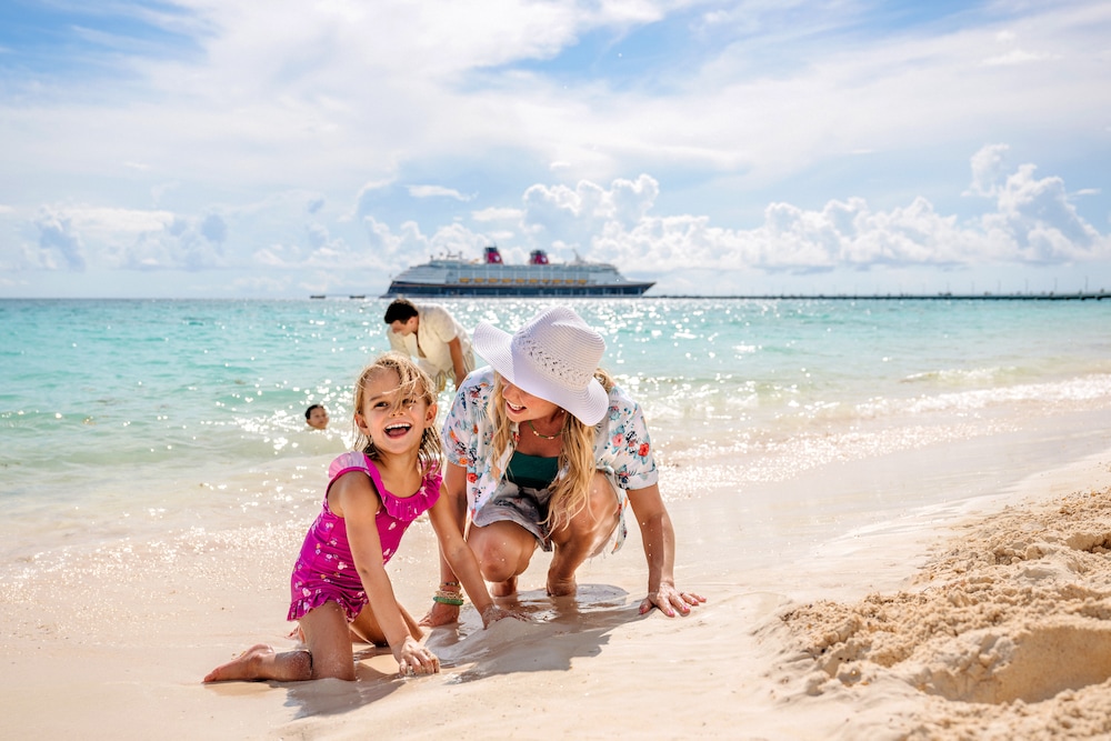 Una familia jugando en la arena en una playa cerca de un barco de Disney Cruise Line