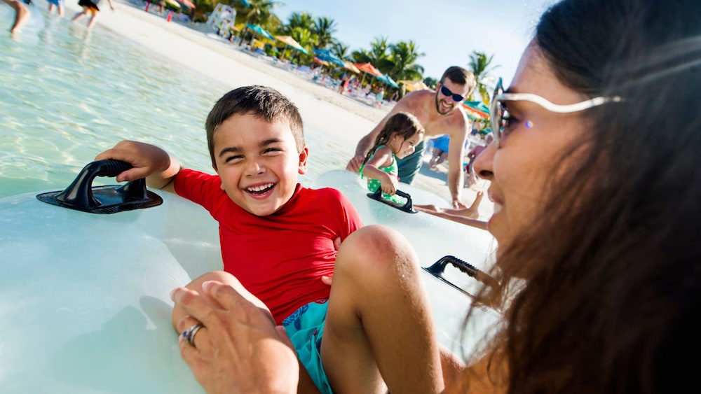 A boy on an inflatable tube next to his mom and other families at Disney's Castaway Cay
