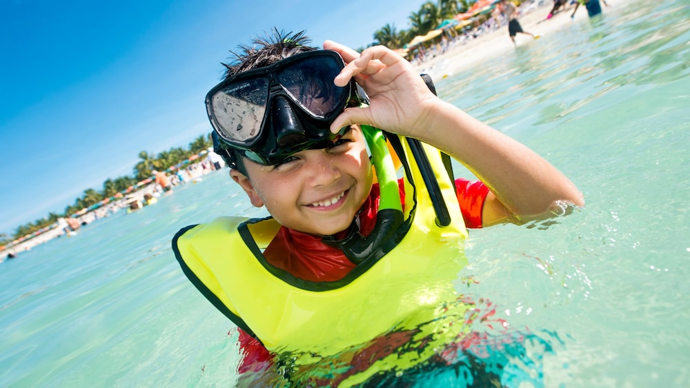 A smiling young boy wearing snorkeling equipment and standing in the sea