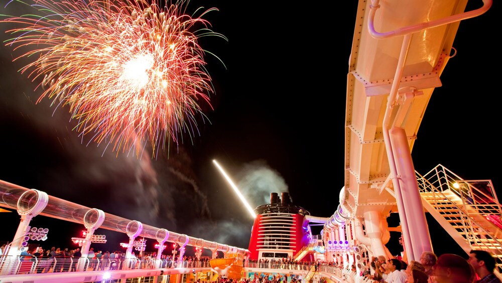 Fireworks illuminating the sky above a Disney cruise ship deck crowded with spectators at night